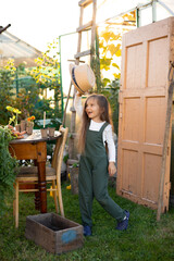 a vertical portrait of a cute funny blue-eyed farmer girl in a hat with long hair and a green...
