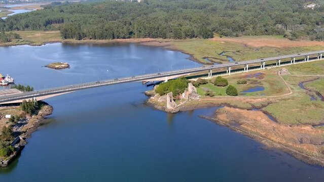 bridge with cars circulating over the Ulla River and the ruins of the towers of the West Viking landing zone, sunny afternoon, drone shooting traveling forward zenithal. Catoira, Galicia, Spain