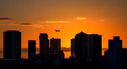 Fototapeta na wymiar Airliner Departing a City at Sunset with Buildings Silhouetted.