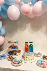 Gender party, blue and pink balloons on the background, close-up of a festive table with cake, lemonades, donuts and pretzels