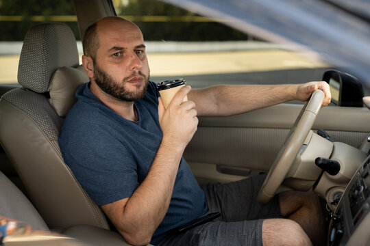 Handsome man dressed cassual in blue t-shirt driving a car with coffee to go