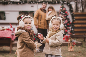Mom, dad and two little twin daughters dressed in stylish fur coats and winter fur headphones play...