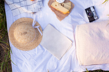Mock up of newspaper lying on a picnic blanket with cheese, camera and straw hat, top view. Concept of leisure, reading and summer. Copy space. News on vacation. Summertime reading.