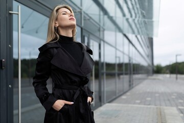 portrait of a middle-aged businesswoman woman in a strict black business style against the background of a glass facade of a business center