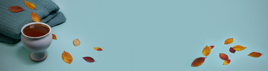 leaves, a blanket and a cup of tea on a blue background. keep warm on a cold day. winter is coming soon.