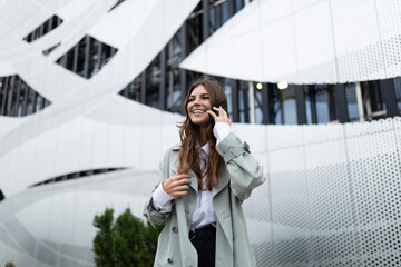 young beautiful woman talking on a mobile phone in stylish clothes on the background of a modern building