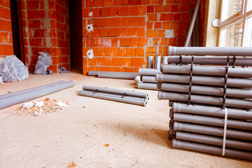 Pile of sewerage tubes placed on the floor in the unfinished residential edifice
