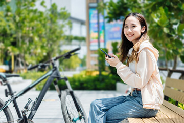 Beautiful Asian woman listening favourite music on headphones from mobile phone, Happiness relaxation summer in park with music riding bicycle in green park.