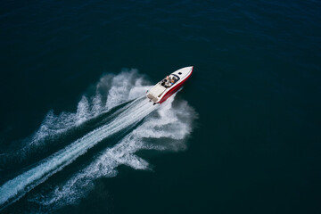 Luxurious Red White motorboat rushes through the waves of the blue Sea. Boat fast moving aerial view. Luxurious boat fast movement on dark water.