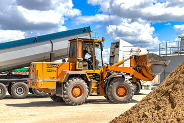 A large front loader transports crushed stone or gravel in a bucket at a construction site or concrete plant. Transportation of bulk materials. Construction equipment. Bulk cargo transportation.