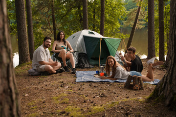 Photo of four friends hiking and camping together in summer woods in daytime.