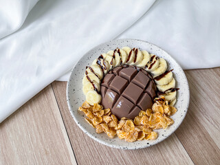 Chocolate milk pudding with toppings. A bowl of chocolate milk pudding with banana and cornflakes, topped with chocolate sauce.
