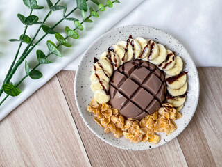 Chocolate milk pudding with toppings. A bowl of chocolate milk pudding with banana and cornflakes, topped with chocolate sauce.