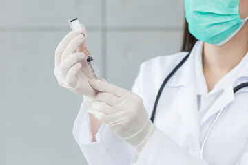 Woman doctor is using syringe to suck vaccine (Coronavirus vaccine) from bottle while her hands...