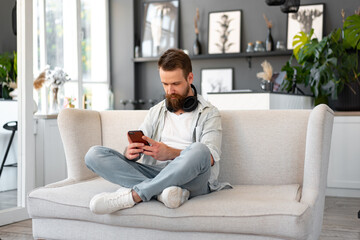 Obraz premium Handsome young bearded man spending time at home with phone in hands.