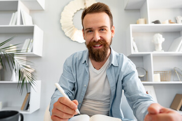 Young bearded man sitting at the desk and taking notes at home