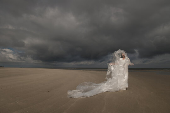 abstract art portrait of woman in white dress and sheet of plastic dancing on the beach under cloudy sky