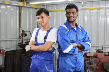Multiethnic technicain mechanic crossed arms with confident while working on metal lathe machine operate polishing car disc brake at garage. Maintenance automotive and inspecting vehicle part concept