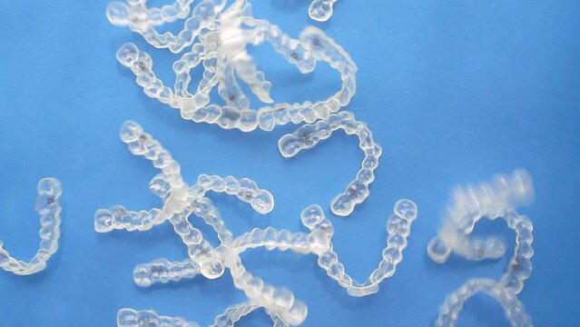 Multiple orthodontic clear aligners fall randomly. Slow motion footage.