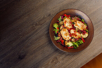 Traditional chicken fillet salad with greenery, pepper, basil, eggplant, vegetables and garnet on plate on table in cafe