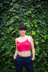 Cool woman with her hair tied up posing while looking at the camera in a garden