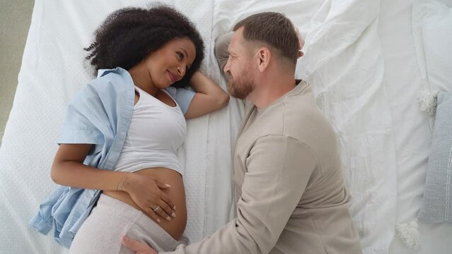 Top view pregnant couple lying in bed, together waiting for childbirth. Tender care of husband to his girlfriend.