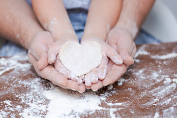 Top view father and child's hand, cut out heart shaped cookies from dough on hands on the background of a wooden table with loose flour. Flat failure. - obrazy, fototapety, plakaty