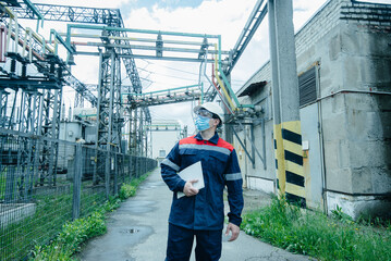A masked power engineer during a pandemic inspects the modern equipment of an electrical substation before commissioning. Energy and industry. Scheduled repair of electrical equipment.