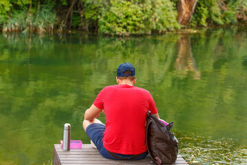 Man sitting back. An adult man resting in shade on shores lake was bleeding on beautiful sunny...