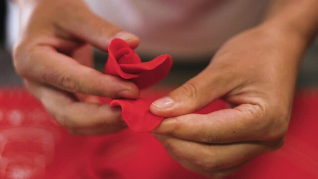 Close-up of a woman handcrafting a red rose to decorate a cake