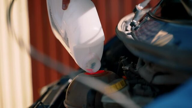 car maintenance, a man pours fresh antifreeze into the engine. Antifreeze, pink coolant, canister.