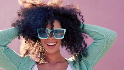 Black woman with sunglasses smile, play with hair and laugh against pink backdrop in sunshine. Model girl with curly afro hair, happy with blue fashion glasses against color wall or background - Powered by Adobe