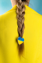 Fototapeta na wymiar Women's braid with a heart in the patriotic colors of the Ukrainian flag, yellow and blue. Stop the war in Ukraine. Help save the Ukrainian nation.
