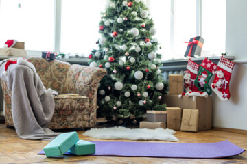 Empty space in fitness center with big windows and natural wooden floor. Unrolled yoga mat on the floor, no people. Decorated christmas tree.