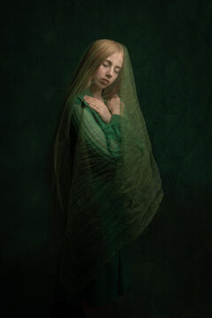 classic painterly studio portrait of a woman in a dark green dress and veil embracing her self