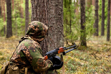 Ukrainian soldier man dressed military camouflage uniform with weapon in forest at nature background, rear view. Male border guard in country border with autogun on war. Copy text space