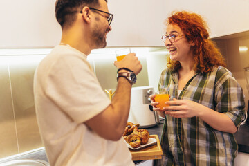 Happy young couple enjoying fresh orange juice for a breakfast at home