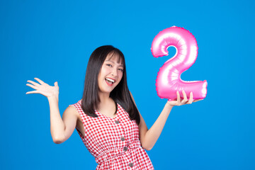 Happy new year and Merry Christmas concept. Beautiful young asian woman with balloons number 2 on blue background.