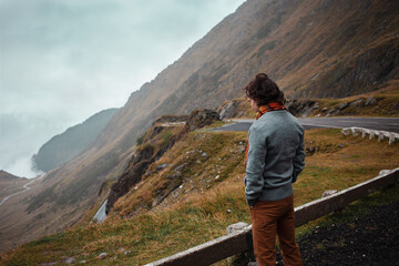 Fototapeta premium man stands on road in mountains in Romania, Carpathians. concept of loneliness, freedom, melancholy and thoughtfulness. Autumn, rain and fog, nature, outdoors. Man and nature, landscape, background.