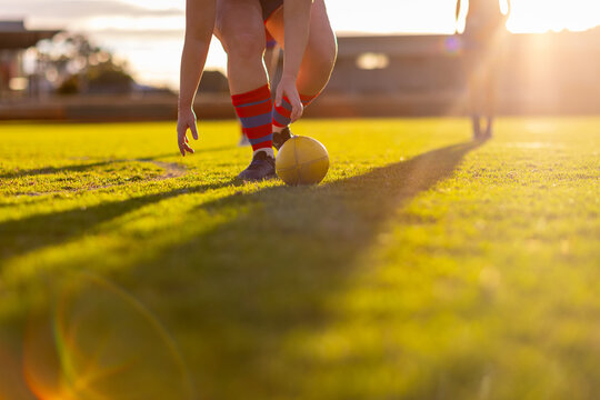 female aussie rules footballer bending to scoop up ball