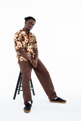 Serious concentraed man with stylish funny hairstyle looking at camera sitting on black chair wearing casual oversized clothes on white background in studio isolated.