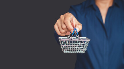 Fototapeta premium A young man is holding a mini shopping cart while standing on a gray background