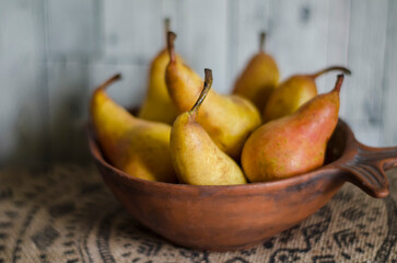 Juicy ripe pears in a clay bowl on a hemp tablecloth with an ornament.