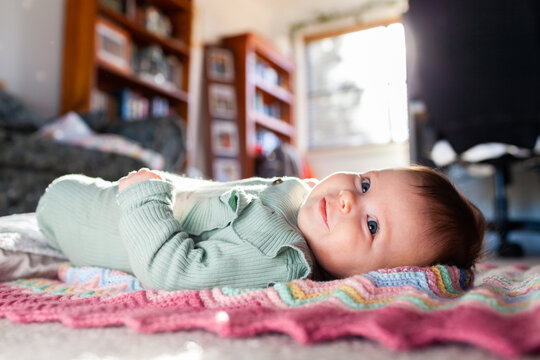happy baby girl lying on blanket on loungeroom floor in winter sunlight