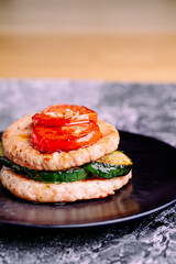 Burger plate with grilled vegetables on a black plate.