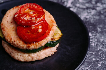 Burger plate with grilled vegetables on a black plate.