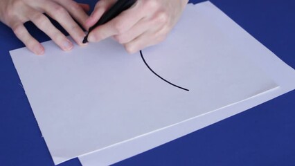 Left-Handed Person Draw A Pisces Symbol On White Paper With A Black Marker. - close up