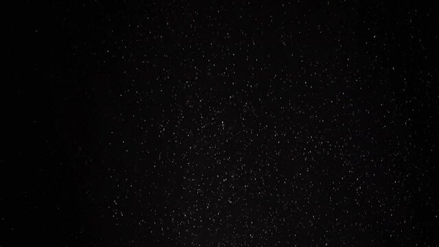 Stream of Slowly Falling Particles of Dust, Debris, Powder on Black Background. Sparks, particles of white powder, flakes rotate, swirl, float in cloud fog. Empty space. Star rain, meteorites. Cosmos.