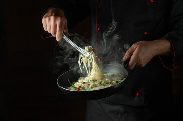The chef cooks spaghetti with spices and seasonings in a steamed hot pan. Space for advertising on...