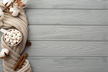 Winter atmosphere concept. Top view photo of mug of hot drinking with marshmallow cotton branch knitted scarf anise and cinnamon sticks on grey wooden desk background with copyspace
